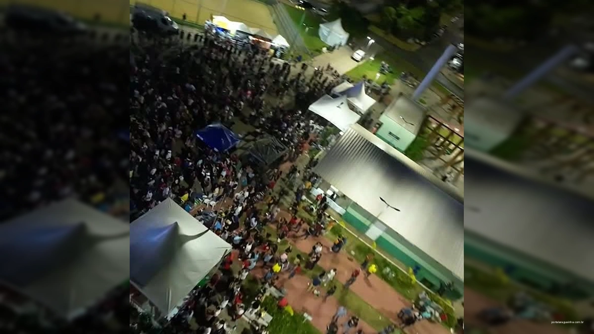 Vista aérea da festa de 31 anos de Cláudia à noite, com palco, multidão e iluminação colorida.