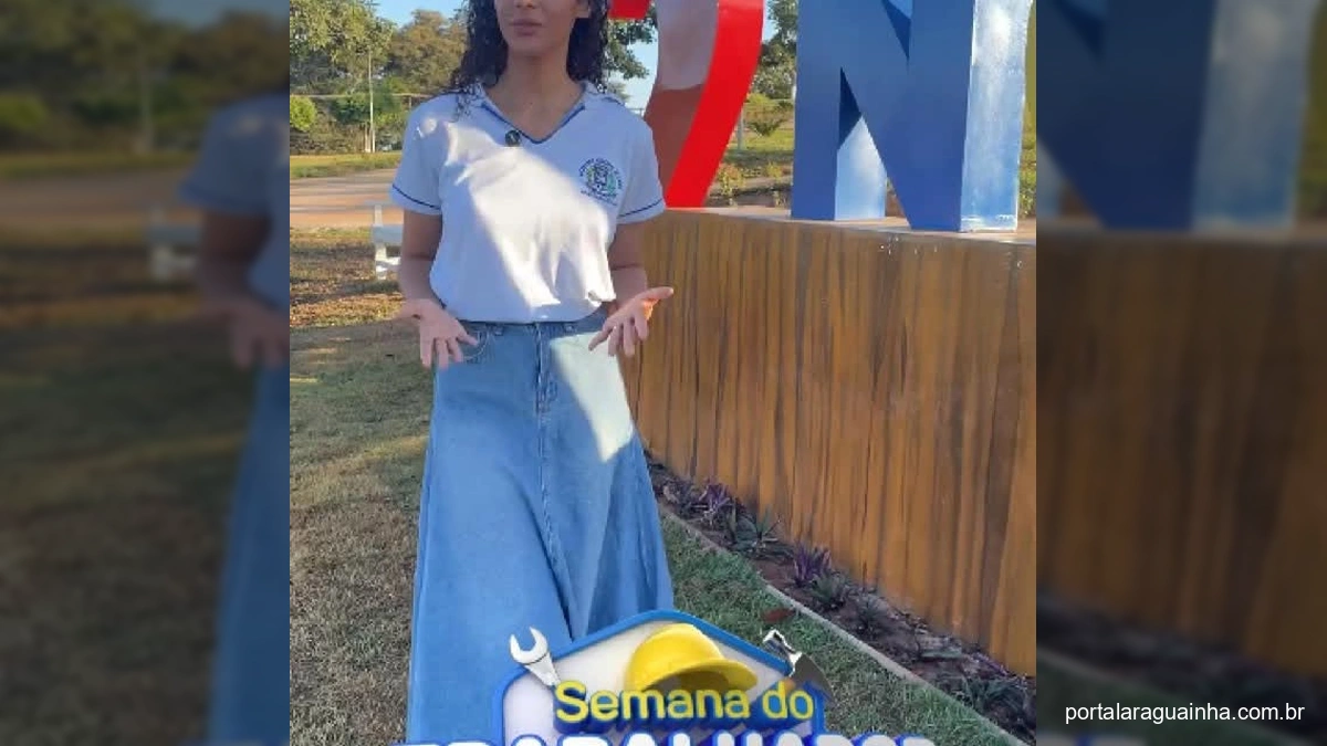Mulher apresentando a Semana do Trabalhador em Nova Bandeirantes, ao lado do letreiro 'Eu Amo Nova Bandeirantes'.